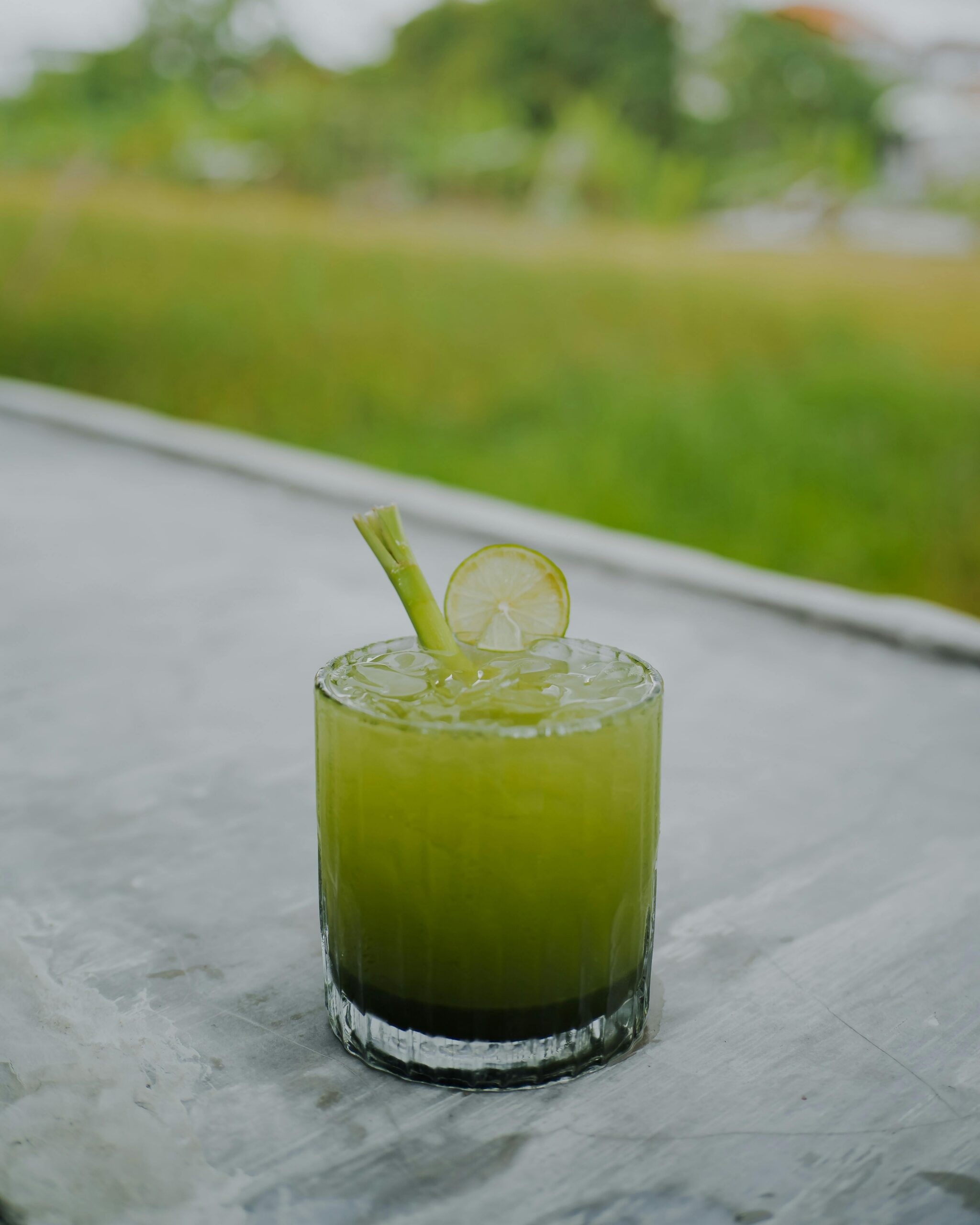 Chilled green cocktail with lime slice and ice cubes on a table outdoors.