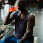 Mature African American man drinking juice during a gym workout session sitting on a wooden box.