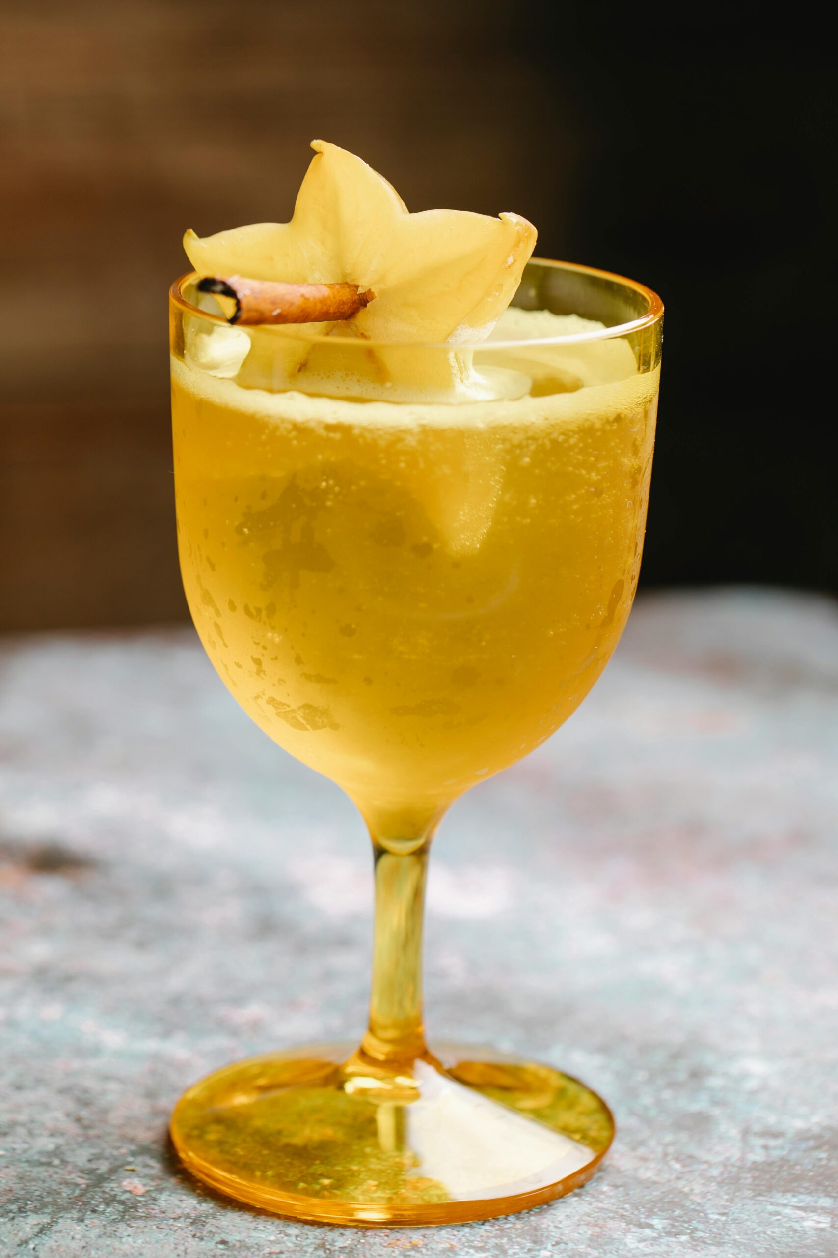 Wineglass filled with fizzy canebar beverage decorated with carambola fruit on cinnamon stick placed on marble table on blurred background in kitchen