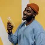 Smiling man holding a nutritious drink indoors against a yellow background.