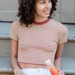 Young woman with curly hair relaxing with a drink while sitting on steps.