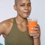 African American woman in a sports bra drinking fresh carrot juice, symbolizing a healthy lifestyle.